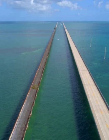 The image shows two long, parallel bridges extending over a vast body of water, under a blue sky with some clouds.